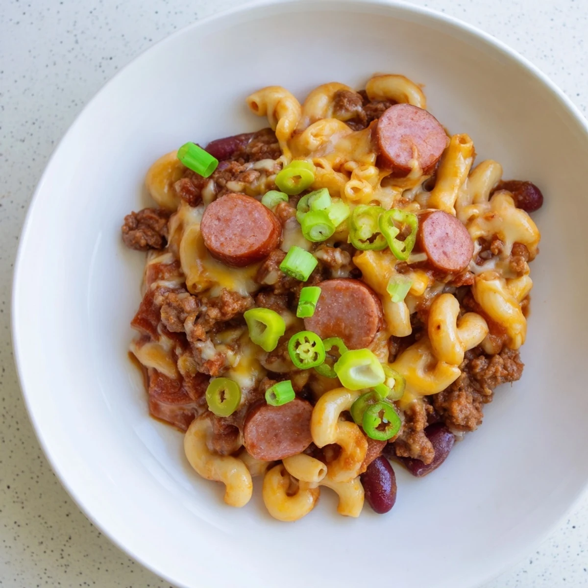 A close-up view of a comforting bowl of Chili Cheese Dog Mac & Cheese, loaded with toppings, ready to eat.
