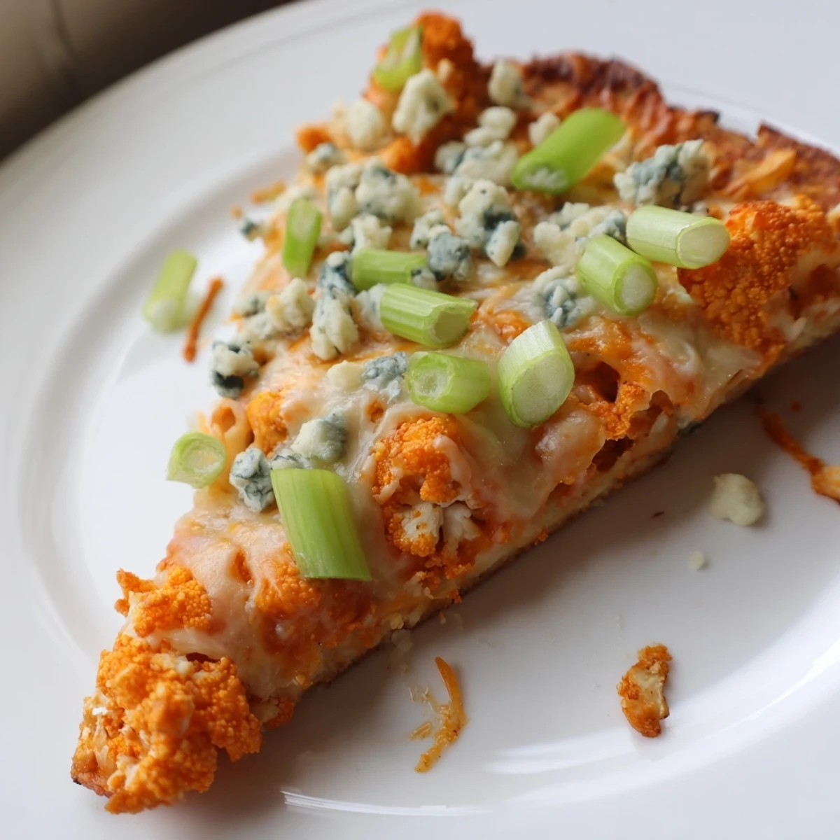 A vibrant Buffalo Cauliflower Pizza rests on a checkered napkin, with buffalo sauce drizzle and celery garnish nearby.