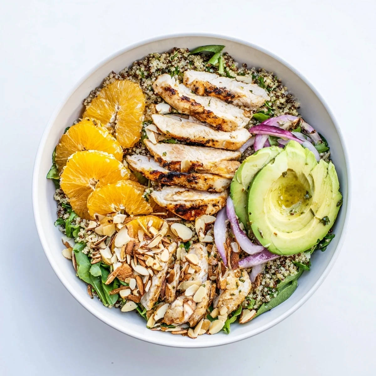 Grilled herb chicken sits atop a vibrant salad of quinoa, mixed greens, and creamy avocado slices.