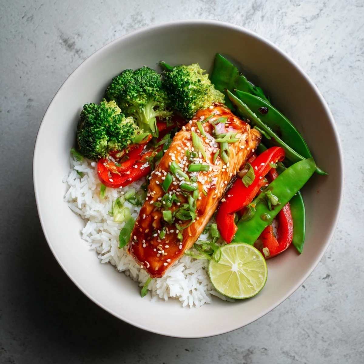 Glossy maple soy glazed salmon fillets rest on fluffy rice beside bright broccoli and snap peas, garnished with sesame seeds and green onions.