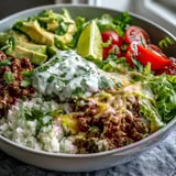 A close-up of a Low Carb Burrito Bowl features juicy ground beef, fresh diced tomatoes, and a dollop of sour cream.
