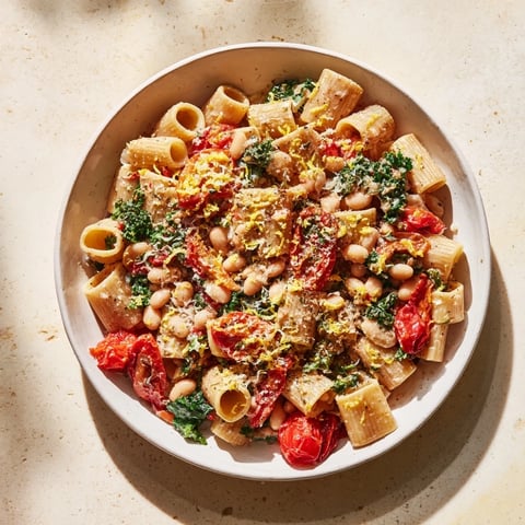 Steaming bowl of Healthy Tuscan White Bean & Kale Christmas Pasta, garnished with lemon zest, ready to savor.