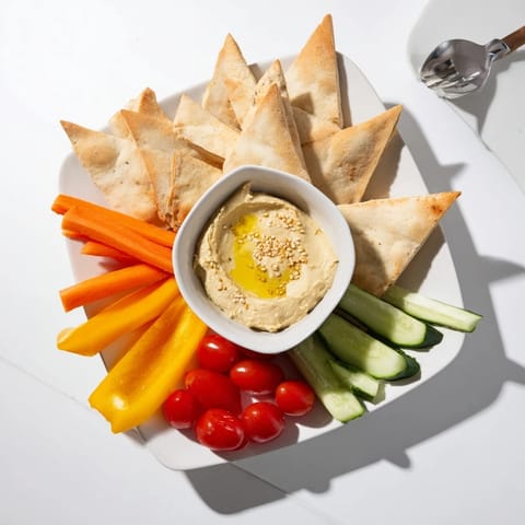 A close-up of creamy DIY hummus, golden pita wedges, and colorful vegetable sticks for snacking.