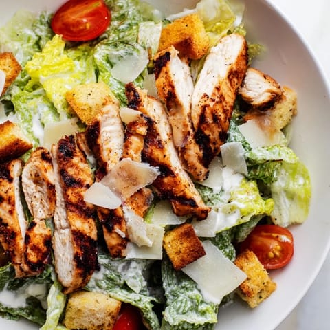 A close-up view shows golden-brown chicken and shaved Parmesan on a fresh salad, highlighting the vibrant colors of the Yogurt Caesar Grilled Chicken Salad.  