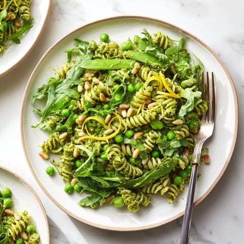 A close-up of Spring Green Pesto Pasta Salad served chilled with toasted pine nuts and a bright lemon zest.