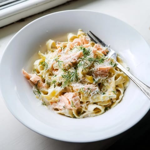 Flaky hot-smoked salmon nestled in silky pasta, garnished with chopped herbs and black pepper for a bright, savory aroma.