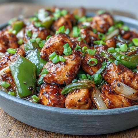A steaming bowl of Black Pepper Chicken served over white rice with scallions, perfect for a quick weeknight dinner.  