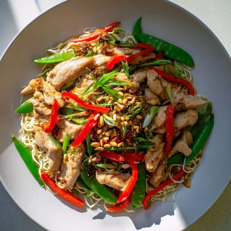 A steaming bowl of Mongolian Chicken with its savory sauce ladled over delicate rice noodles.