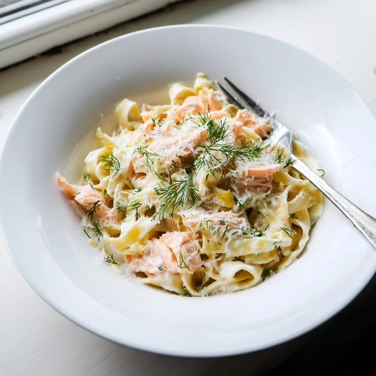Flaky hot-smoked salmon nestled in silky pasta, garnished with chopped herbs and black pepper for a bright, savory aroma.