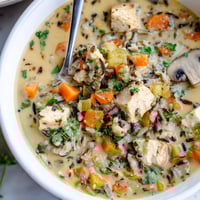 Creamy Parmesan Mushroom Chicken and Wild Rice Soup steaming in a rustic bowl, garnished with fresh parsley and extra grated cheese for a cozy dinner.  